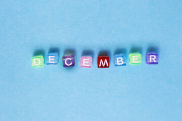 inscription december made by multicolor plastic cubes on a blue background.