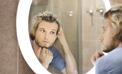 young man looking in the mirror,combing his hair,looking at problems on face.