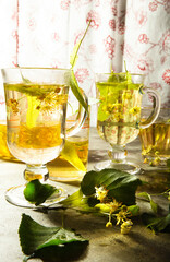 Two glass cups of freshly made yellow linden tea with leaves and flowers of linden tree.