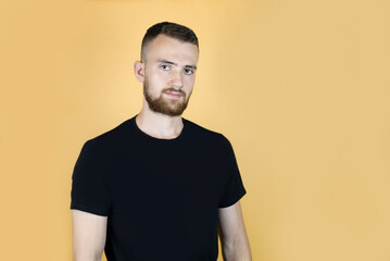 A young man with a beard on an orange background with a calm, slightly sad face, he is troubled by the recent disturbing events in the world, but there is hope in his eyes