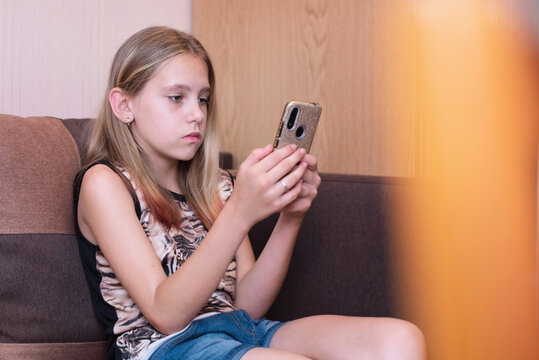 A Young Girl At Home Looks Sadly At The Phone, Plays A Game With Friend Online Instead Of Walking In The Fresh Air In The Park. The Girl Needs A Break From The Phone And All The Gadgets