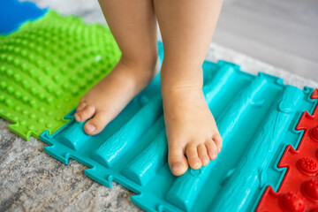 Close up view of Little girl walks on a massage mat. Toddler baby foot massage mat. Exercises for legs orthopedic massage carpet. 