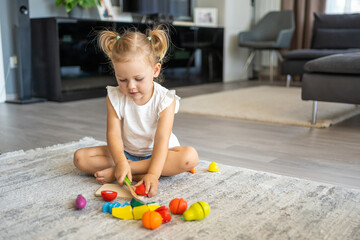 Cute little toddler girl playing at home with eco wooden toys. Happy child cutting vegetables and...