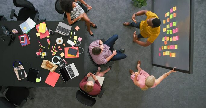 Teamwork of successful businesspeople meeting together from above, cheering with high five gesture after completing visual aid brainstorm. Diverse group of marketing agents planning workshop strategy