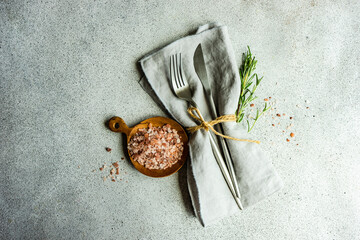 Overhead view of a rustic cutlery setting on a napkin with pink Himalayan salt with fresh rosemary