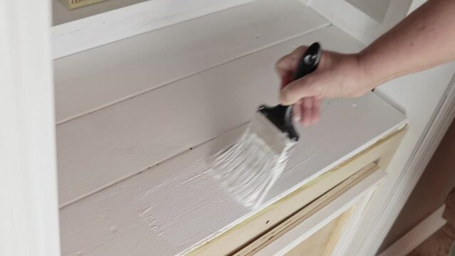 Painting a newly constructed bookshelf home improvement project with a paintbrush and white paint