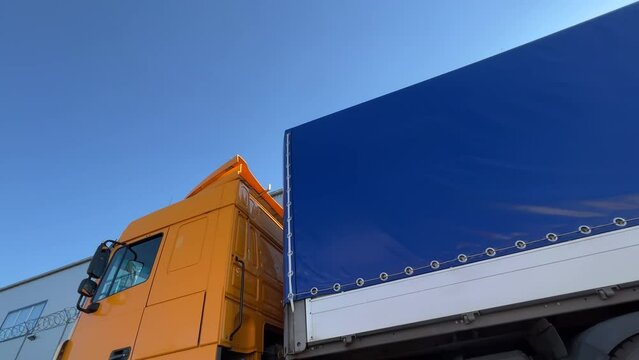 Semi-trailer truck with orange cabin is parked in a logistics park waiting to unload and load goods. Side view. Extreme wide angle shot