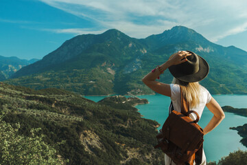 Back view of wanderlust woman with backpack looking at scenic view of lake and mountains from a view point.