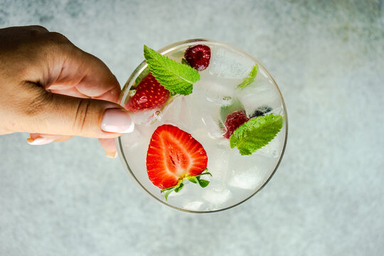 Woman reaching for a summer cocktail with fresh raspberries and strawberries in a champagne coupe