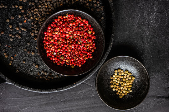 Overhead view of bowls of pink, white and black peppercorns on a table