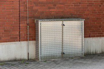 Locked off metal box by a building containing electrical equipment.