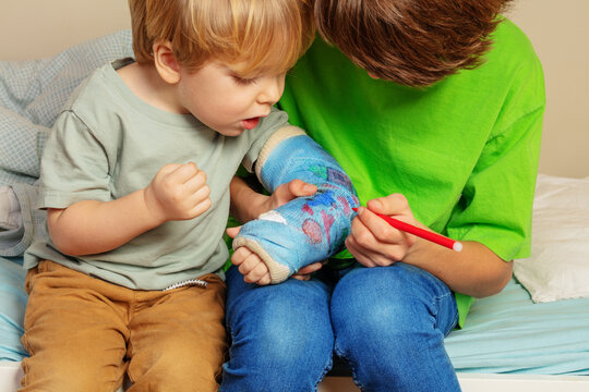 Interested boy look at brother draw on his broken hand cast