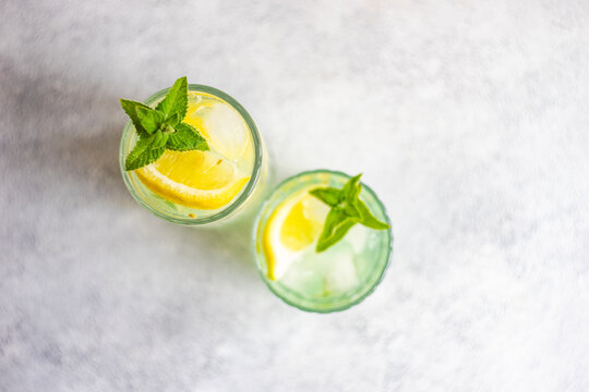 Overhead view of two mojito cocktails on a table with fresh mint and lemon