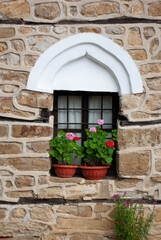 Fototapeta na wymiar A village in Arbanasi, Bulgaria, has rebuilt an old medieval structure of a church and home. You are viewing the stone walls and window trim holding geranium plants, part of a heritage tour.
