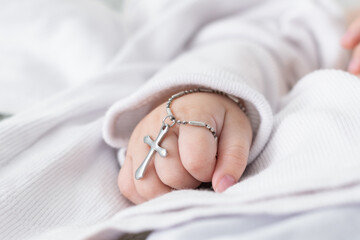 close-up detail of a baby's hand at his baptism, holding a christian cross. catholic baptism in...