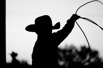 Kid cowboy with lasso for roping in silhouette black and white closeup, authentic western scene.
