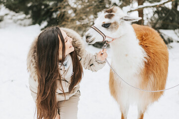 young beautiful woman in fashion stylish winter clothes overall walking and hugging with llama...