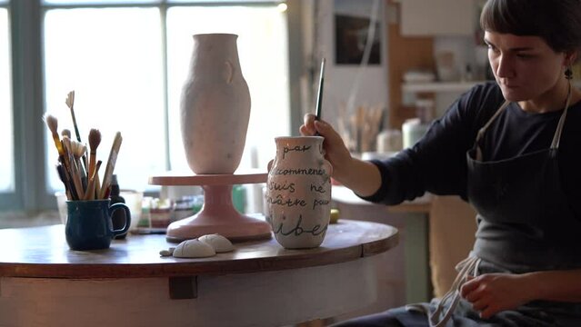 Young craftswoman applies finishing coat to handmade individual product made in studio for sale in interior decor store. Different brushes for painting products on table. Business for self realisation