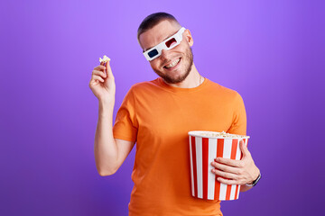 Young caucasian man in 3d glasses eating popcorn