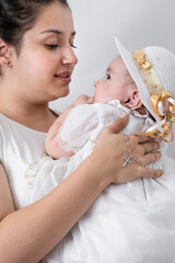 beautiful young latin mother, holding her baby with a silver chain entangled in her hand and with a...