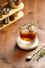 a tumbler glass with brown alcoholic drink, thyme and ice cubes - whisky, rum or cognac - on wooden table, rural scene