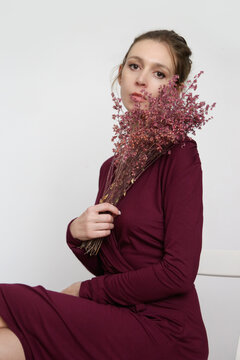 Serie of studio photos of young female model in burgundy wrap dress holding a bouquet of dried red flowers