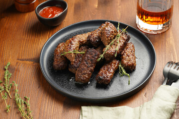 Traditional south european skinless sausages cevapcici made of ground meat and spices on black plate on dark wooden board, with thyme