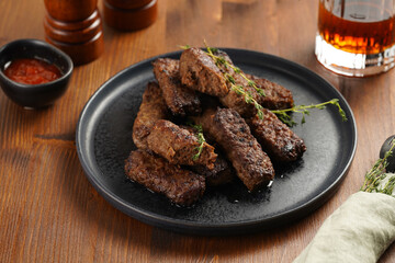 Traditional south european skinless sausages cevapcici made of ground meat and spices on black plate on dark wooden board, with thyme