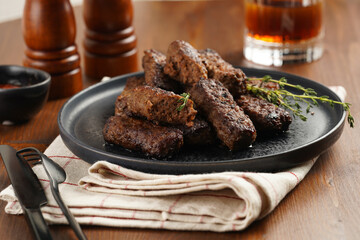 Traditional south european skinless sausages cevapcici made of ground meat and spices on black plate on kitchen towel with thyme