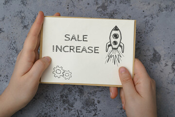 Woman holds card with words Sale Increase on concrete