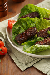 Traditional south european skinless sausages cevapcici made of ground meat and spices on lettuce leaves with thyme and tomatoes on white plate on kitchen towel, black silverware