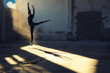 Ballerina jumping and dancing in a dusty abandoned building on a sunny day