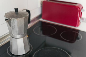 Coffee pot resting on the glass-ceramic hob containing freshly brewed coffee next to a red toaster....