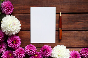 Obraz premium Mock up with blank sheet of paper, pompom dahlias and pen. Copy space for text against dark wooden background. Greeting card for holidays. Floral arrangement. Festive template. Top view