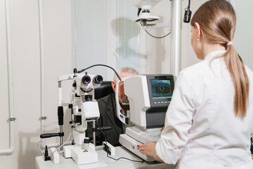 doctor examines elderly man's eye on screen of autorefractometer. 
