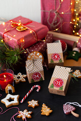 Woman preparing original Advent holiday calendar for Christmas or New year as countdown to Christmas Eve for kids. Zero waste paper package, homemade gingerbread cookies. Cozy home atmosphere