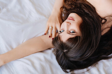 an attractive and sexy young woman with long dark hair lies in bed. bed linen.