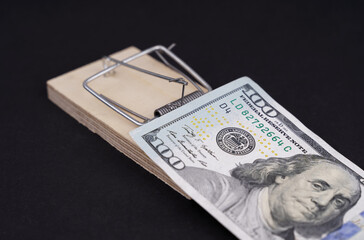 One hundred dollar bill in a wooden mousetrap on a black background.