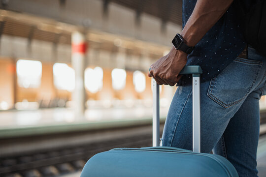 Close up shot of african man holding a suitcase at a train station while he is waiting for train