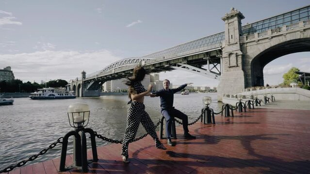 A cool cheerful couple in love on a pier on the river bank. Lovers hold hands and smile