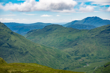 Fototapeta na wymiar View of mountain peaks in the Trossachs National Park from the top of a hill. Beautiful lush green summer mountainous landscape in Scotland