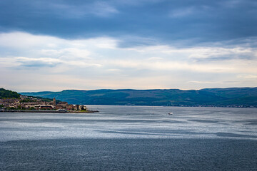 A cape on English coastline with small boat sailing around it and mountain range on the background