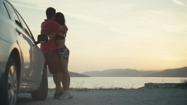 Loving couple hugging at sunset near the car. Happy people vacation on nature by the ocean