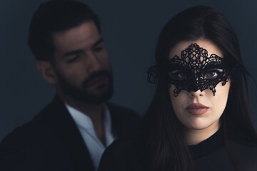 Man in suit looking at woman who wears black lace mask. 