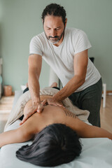 vertical photo of a masseur giving a massage to a patient lying on a massage table. - obrazy, fototapety, plakaty