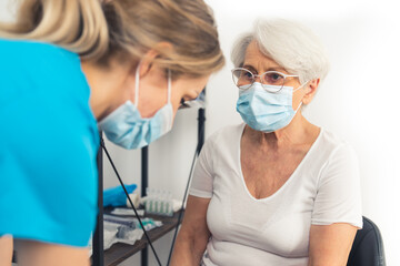 At the doctor's office - an elderly woman and a medical professional with their face masks on. High...