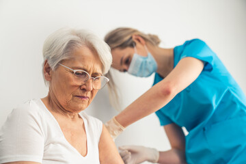 Fototapeta premium Young nurse making the injection of medication or anti-covid vaccine to a senior gray-haired woman at the hospital. High quality photo