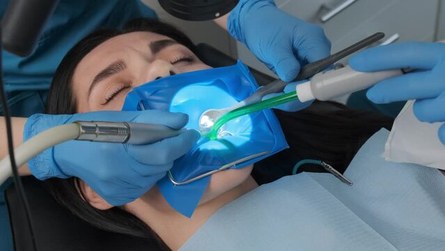 Dentist performs dental procedure on caucasian female patient with dental turbine handpiece, mirror and saliva ejector