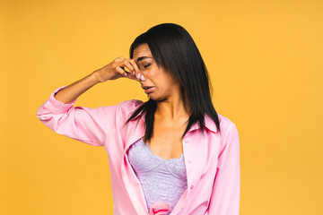 Beautiful hispanic woman standing over isolated over yellow background smelling something stinky and disgusting, intolerable smell, holding breath with fingers on nose. bad smell.