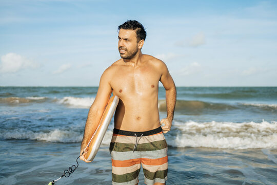 Portrait of Brazilian surfer standing at the beach with his bodyboard. Sport and water sport concept.